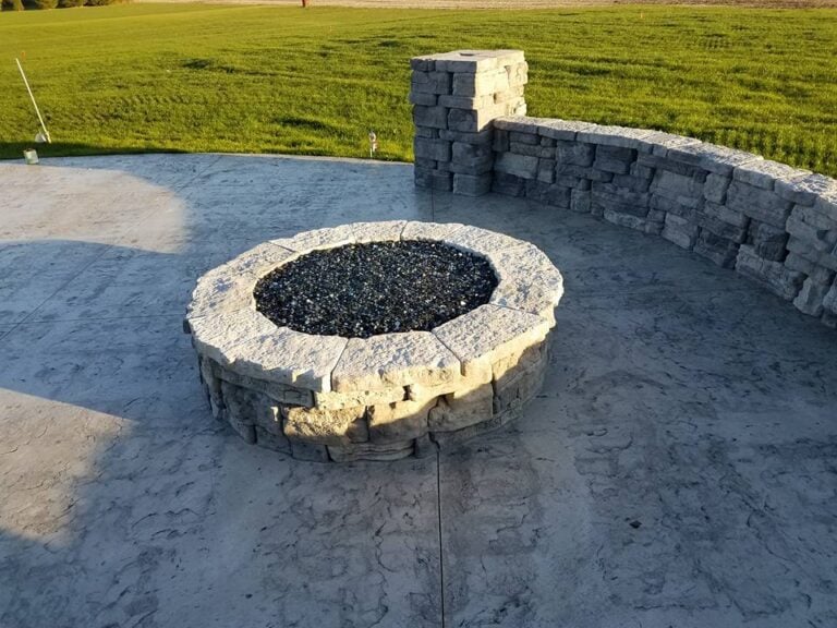 Custom stone fire pit with a curved retaining wall on a stamped concrete patio in Cedar Rapids, IA. Professionally designed outdoor living space perfect for backyard gatherings, relaxation, and entertainment. Expert hardscaping installation using durable stone materials for a long-lasting and stylish outdoor feature.
