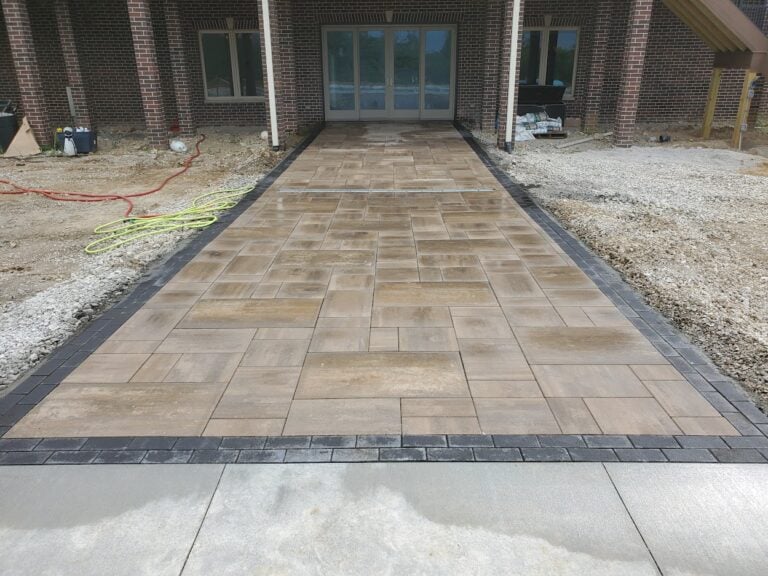 Custom paver walkway with contrasting border leading to a brick home entrance in Cedar Rapids, IA. Professionally installed hardscape design featuring durable, low-maintenance patio pavers for a stylish and functional outdoor space.
