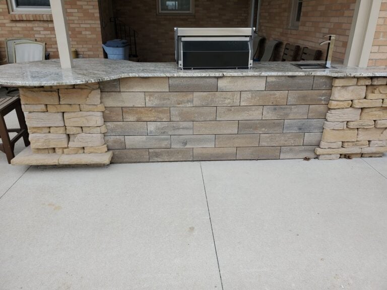 Custom outdoor kitchen with stone veneer and granite countertop. Features a built-in grill, sink, and spacious bar seating area, perfect for backyard entertaining.
