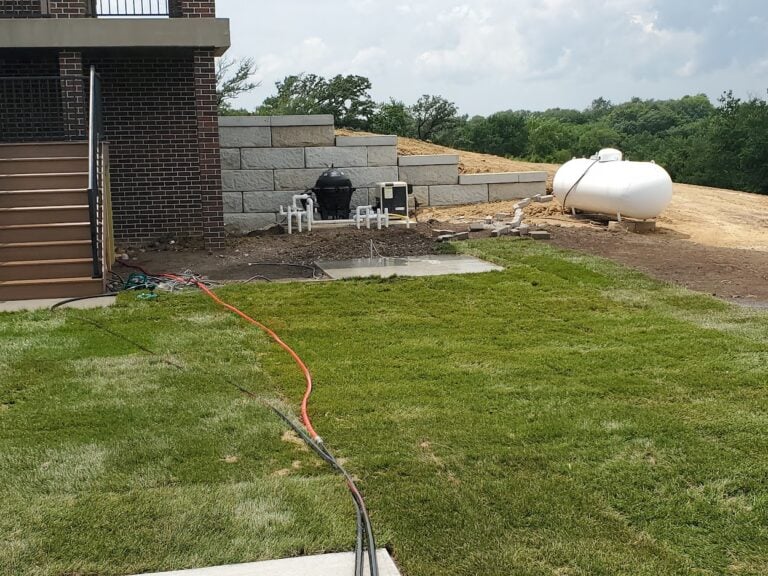 Large concrete block retaining wall installation in Cedar Rapids, IA, designed for erosion control and landscape stabilization. The professionally built hardscape supports a sloped backyard with fresh sod installation, enhancing outdoor functionality and aesthetics. Expert retaining wall construction for long-term durability and property enhancement.