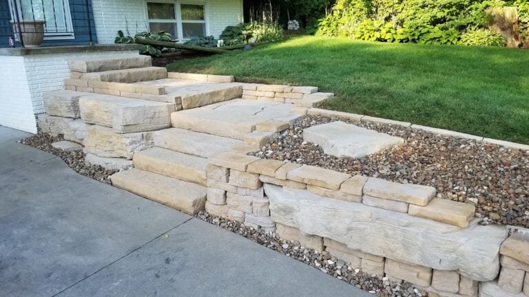 Natural stone steps and retaining wall with a tiered landscape design. Expertly crafted hardscape enhances curb appeal and provides a durable, stylish entryway.
