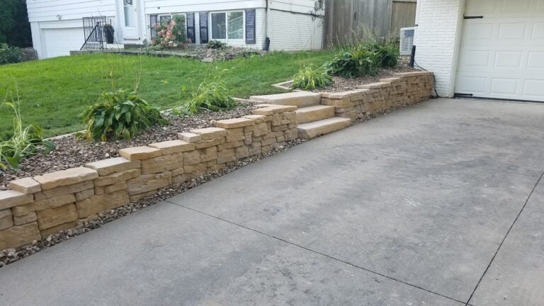 Custom stone retaining wall with integrated steps for a functional and elegant landscape design. Professionally built hardscape enhances curb appeal and soil retention.