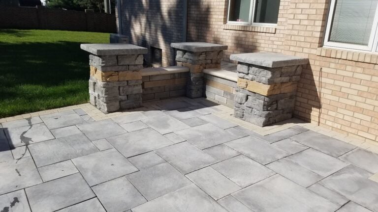 Modern paver patio with built-in stone seating walls and pillars, enhancing outdoor living space. High-quality hardscaping for durability and elegance in backyard design.