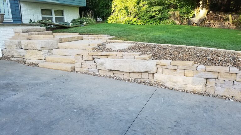 Natural stone retaining wall with integrated steps, enhancing curb appeal and preventing soil erosion. Expertly crafted hardscape design for a durable and stylish landscape transformation.