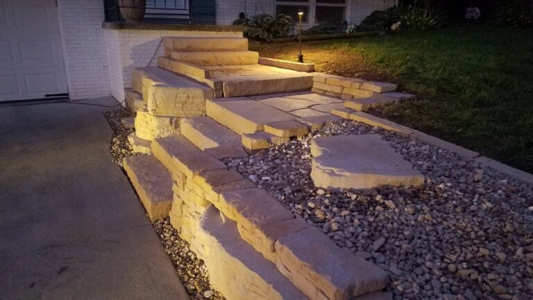Elegant natural stone walkway and steps with built-in landscape lighting, enhancing curb appeal and safety. Professionally designed hardscape for a timeless and functional outdoor entryway.