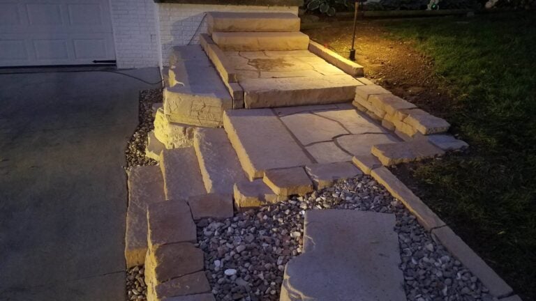Custom natural stone walkway and steps with integrated landscape lighting, creating a warm and inviting entrance. Expertly designed hardscape enhances curb appeal and outdoor functionality.