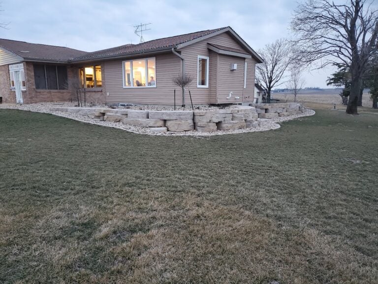 Custom limestone retaining wall installation in Cedar Rapids, IA, designed to enhance curb appeal and prevent soil erosion. The tiered landscape features natural stone blocks with decorative rock for a low-maintenance and stylish outdoor space. Professionally built hardscape solution for improved property aesthetics and stability.