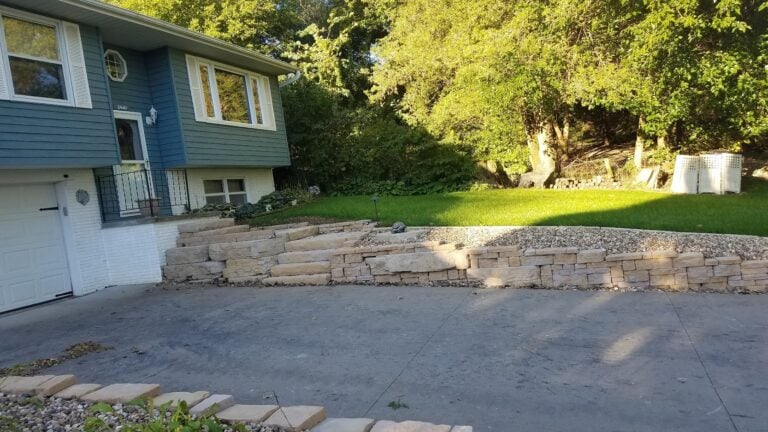 Custom stone retaining wall with integrated steps leading to a beautifully landscaped front yard. Hardscape design enhances curb appeal and prevents soil erosion for a functional and stylish outdoor space.