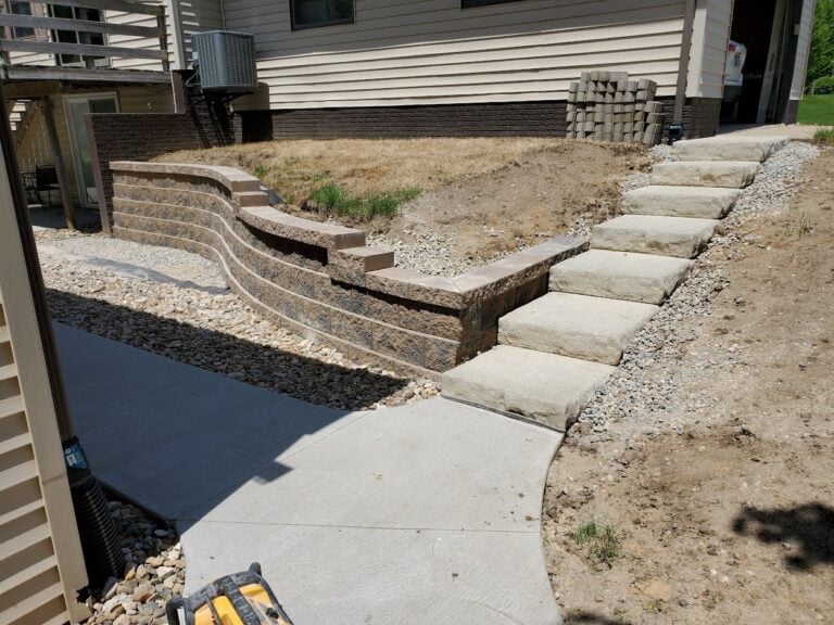 Curved retaining wall with integrated stone steps and concrete walkway in Des Moines, IA. Designed for erosion control and improved accessibility, this hardscape project enhances both function and curb appeal.