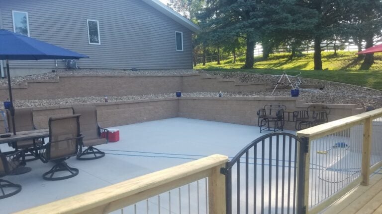 Spacious backyard patio with retaining walls and built-in seating, perfect for outdoor entertaining. Featuring a modern concrete surface, decorative stone accents, and comfortable patio furniture.