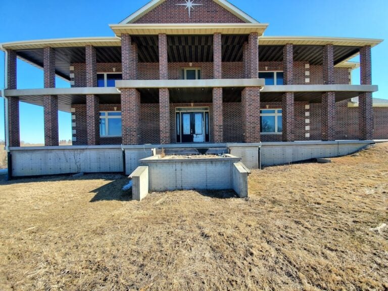 Large brick home under construction with expansive balconies and a partially built retaining wall. Open framework and unfinished landscaping highlight the potential for a grand outdoor space.