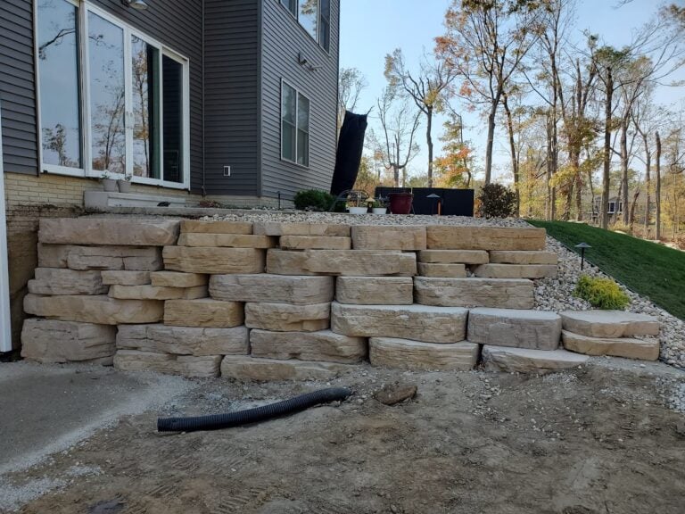 Custom limestone retaining wall installation in Cedar Rapids, IA, designed for erosion control and enhanced outdoor aesthetics. The multi-tiered natural stone wall supports a raised landscape bed with decorative rock and plants, providing a durable and visually appealing hardscape solution for sloped yards.