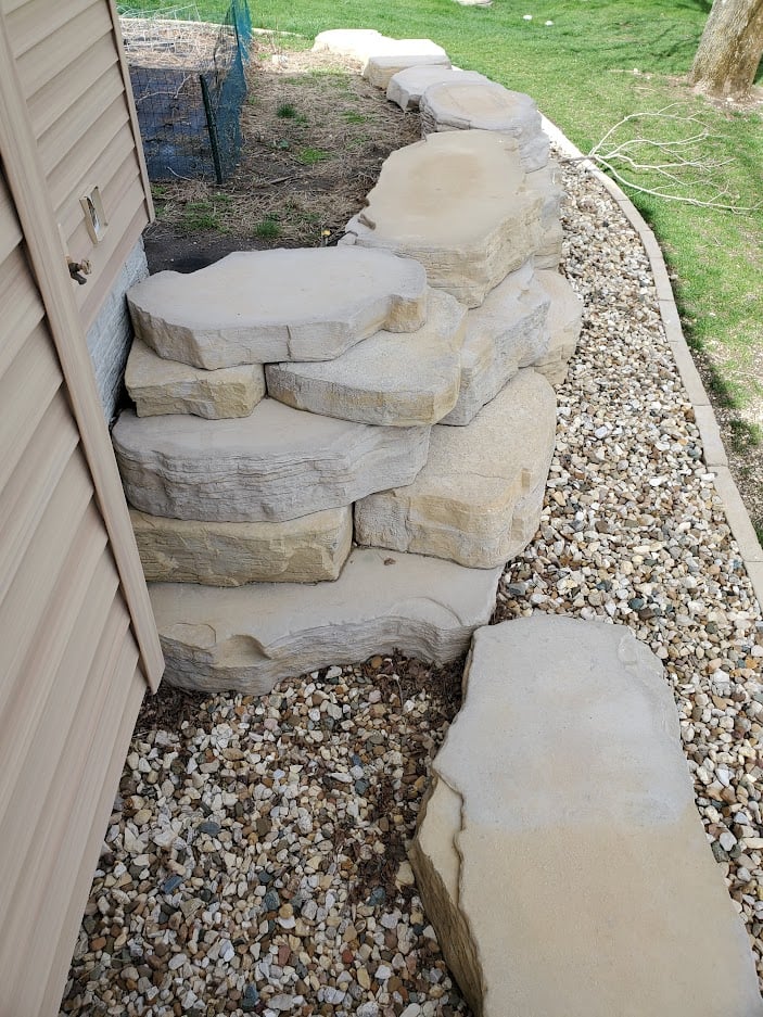 Custom limestone boulder staircase with natural stone retaining wall and decorative river rock landscaping. Functional hardscape design for erosion control and easy backyard access.