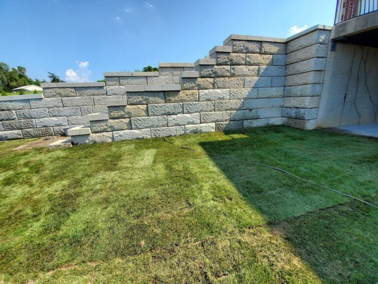 Tiered concrete block retaining wall installation in Cedar Rapids, IA, designed for erosion control and landscape support. Freshly laid sod enhances the outdoor space, providing a functional and visually appealing backyard solution. Expert hardscaping and grading services for sloped properties.