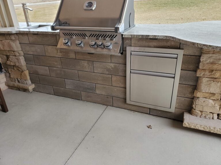 Luxury outdoor kitchen with built-in stainless steel grill, storage drawers, and stone veneer finish. Granite countertop adds durability and style for backyard cooking and entertaining.