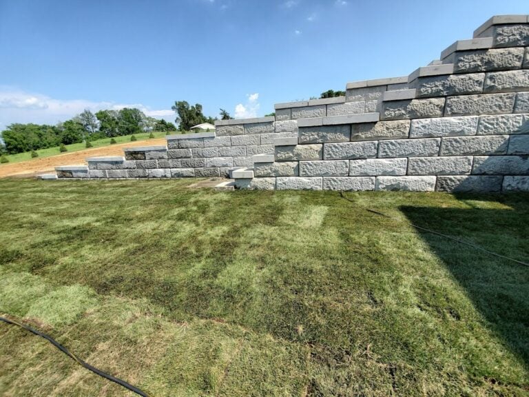 Large-tiered retaining wall installation in Cedar Rapids, IA, built with durable concrete blocks for erosion control and landscape stabilization. The newly laid sod enhances the backyard's functionality, creating a structured and visually appealing outdoor space. Expert hardscaping solution for sloped yards and property enhancement.