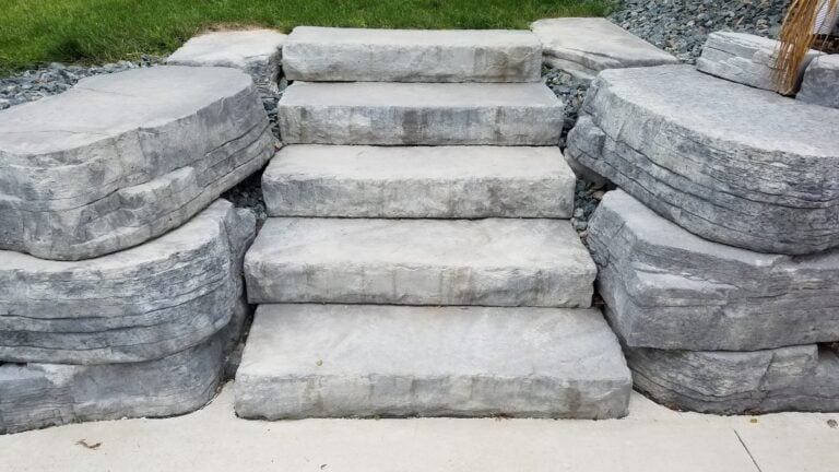 Natural stone steps with large boulder retaining walls create a durable and visually appealing outdoor stairway. Expertly crafted hardscape design enhances functionality and curb appeal.