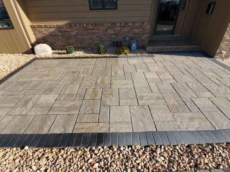 Close-up view of a custom stamped concrete front patio in Cedar Rapids, IA, featuring a textured stone pattern with a contrasting dark border. The professionally installed hardscape enhances curb appeal and provides a durable, low-maintenance entryway. Expert patio design for long-lasting beauty and functionality.
