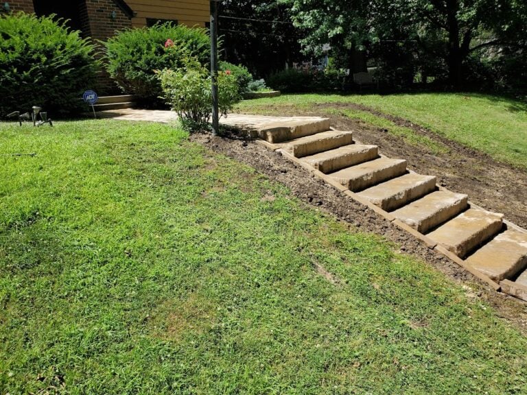 Custom natural stone staircase installation on a sloped lawn in Cedar Rapids, IA. The professionally crafted outdoor steps provide a durable and visually appealing pathway, enhancing accessibility and erosion control in the landscape. Expertly designed hardscaping solution for functional and stylish yard improvements.