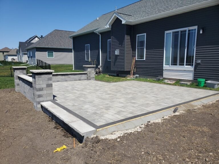 Newly constructed paver patio with a custom retaining wall and pillar accents in Cedar Rapids, IA. The spacious outdoor living area features high-quality interlocking pavers, adding durability and style to the backyard of a modern home. Professionally installed hardscaping for enhanced outdoor entertainment and relaxation.