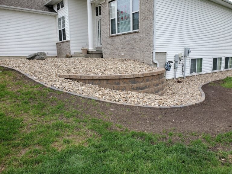 Retaining wall with decorative rock landscaping for erosion control and curb appeal. This professionally designed sloped yard solution enhances drainage and creates a low-maintenance front yard landscape.