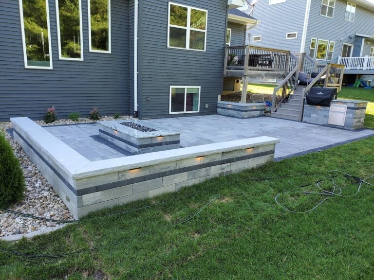 Modern backyard patio with built-in seating wall and fire pit in Cedar Rapids, IA. Sleek paver design with integrated LED lighting, perfect for outdoor entertaining and relaxation.