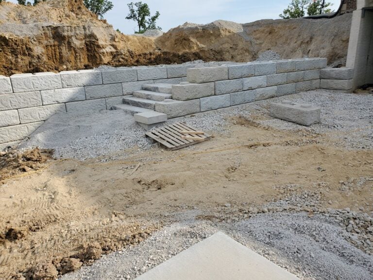 Ongoing retaining wall construction with limestone blocks and integrated steps in Cedar Rapids, IA. Professional hardscape installation for erosion control, landscape elevation, and structural support.