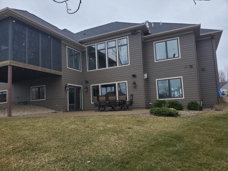 Backyard patio and landscaping of a modern two-story home in Cedar Rapids, IA. The outdoor space features a spacious concrete patio with outdoor dining furniture, a screened-in porch, and well-maintained shrub landscaping. Professionally designed for functionality, curb appeal, and outdoor relaxation.