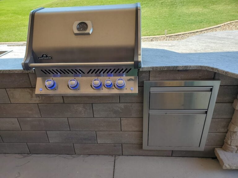 Custom outdoor kitchen with built-in Napoleon stainless steel grill and storage drawers. Perfect for backyard barbecues and entertaining with a durable stone countertop and modern design.
