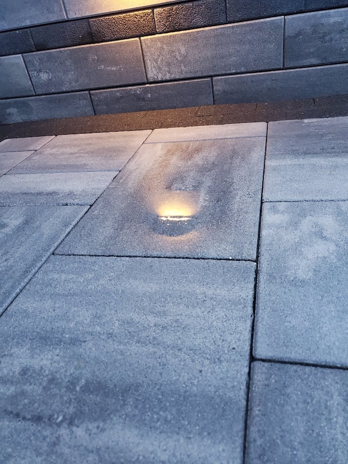 Modern outdoor paver patio with integrated LED step lighting for enhanced nighttime ambiance and safety. Durable hardscape design with sleek retaining wall for a stylish backyard upgrade.